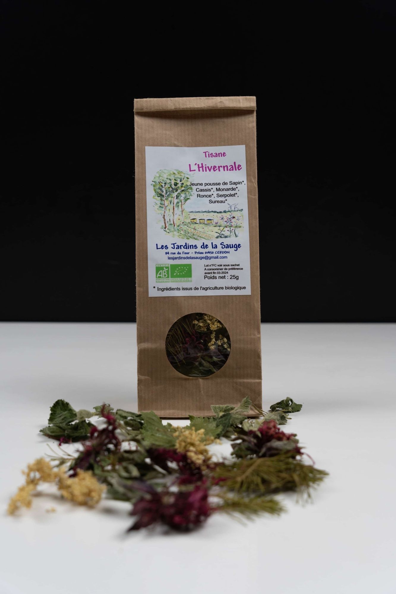 La tisane L'Hivernale des Jardins de la Sauge dans son sachet kraft étiqueté, devant les plantes séchées qui la composent.