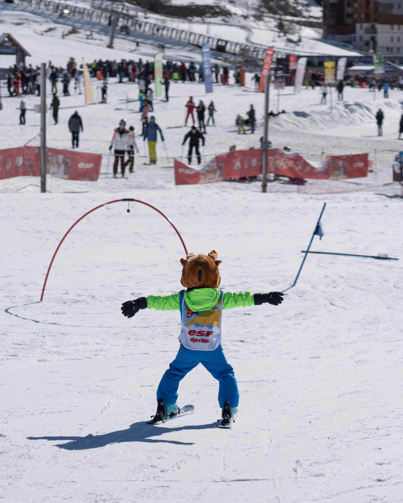 Un enfant déguisé en mascotte descend la piste de l'école de ski de l'Alpe d'Huez, devant la foule du front de neige.